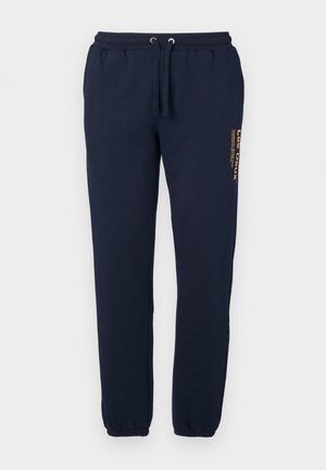 Navy blue sweatpants made of cotton blend fabric, featuring an elastic waistband with drawstring and elastic cuffs. A logo is printed on the side.