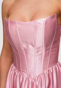 Robe rose en satin sans bretelles avec baleines visibles sur le corsage ajusté et jupe froncée, portée par une personne montrant les épaules et le haut des bras.