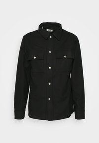 Veste-chemise noire à manches longues avec col, boutons-pression sur le devant, et deux poches poitrine à rabat avec fermeture à pression, présentée sur un fond blanc.