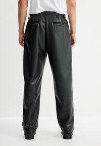 Pantaloni in ecopelle nera con una vestibilità ampia, dotati di tasche posteriori e una superficie liscia. La vita è cucita per garantire comfort.
