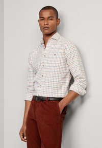 Witte geruite shirt met een blauw en rood patroon, button-down kraag, opgerolde mouwen. Gepaarde met roestkleurige corduroy broek en een zwarte riem.