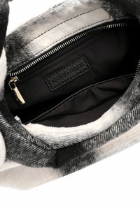 Grau- und weiß gemusterter Innenraum einer Handtasche mit schwarzem Stofffutter, Reißverschlusstasche und einem Etikett. Weiche Textur mit strukturierter Form.