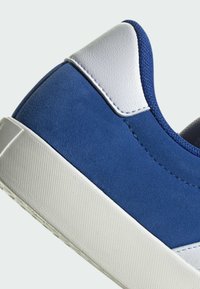 Blå mockaskor med vita läderdetaljer, texturerad gummisula och kontrasterande sömmar. Rund tå och lågprofil design.