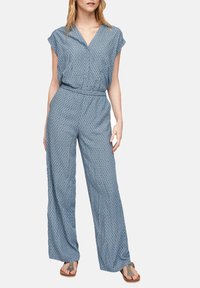 Combinaison bleue à motifs avec manches courtes, col en V, taille élastique et silhouette à jambes larges. Confectionnée en tissu léger.