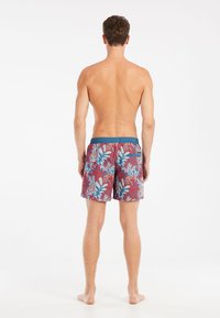 Heren zwemshorts van een rode stof met blauw en witte tropische bladmotieven, elastische tailleband en een achterzak.