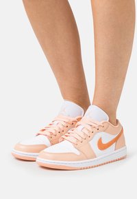 Baskets légères en cuir pêche et blanc, avec un bout perforé, des lacets, et un logo swoosh orange sur le côté.