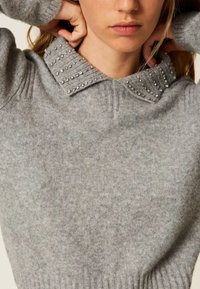 Maglione grigio lavorato a maglia con un colletto strutturato decorato con borchie argentate, materiale morbido, design aderente e polsini a coste sull'orlo.