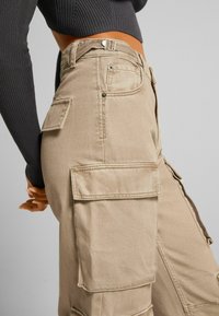 Pantalones cargo color caqui con múltiples bolsillos laterales, costuras reforzadas y una cintura alta, fabricados en un resistente tejido de algodón.