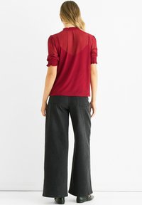 Red sheer blouse with dot pattern, smocked sleeves, and ruffled neckline, paired with wide-leg black denim jeans and black flat shoes.