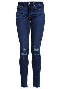 Tmavě modré vysoké skinny džíny s obnošenými roztrženými místy na stehnech a kolenou, s bočními kapsami a zapínáním na knoflík.