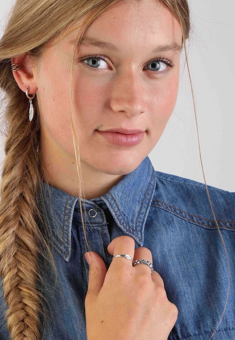 Silberne Ohrringe und Ringe, getragen mit einem Jeanshemd mit spitzem Kragen. Das Hemd ist blau mit sichtbaren Nähdetails.