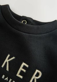 Felpa nera con scollo a costine, caratterizzata da testo bianco ricamato e un piccolo dettaglio metallico sul retro. Tessuto morbido, materiale leggero.