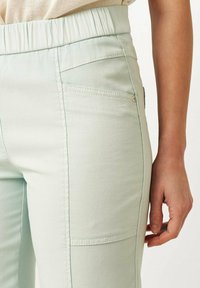 Lichtgroene broek met een gestructureerde stof, voorzien van een elastische tailleband, zijzakken en een slanke, aansluitende pasvorm.