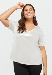 Tricou alb, lucios, cu mânecă scurtă și decolteu în V, având o textură netedă și o croială lejeră. Purtați-l cu colanți negri.