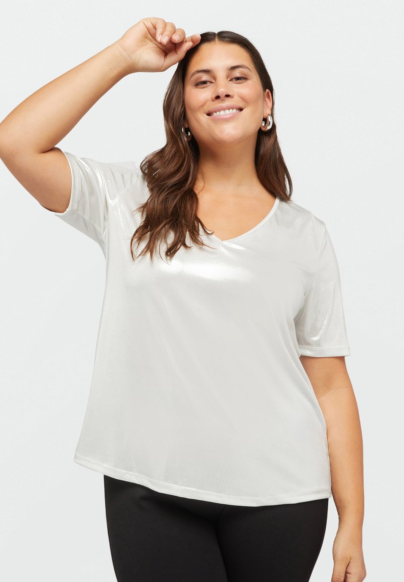 Tricou alb, lucios, cu mânecă scurtă și decolteu în V, având o textură netedă și o croială lejeră. Purtați-l cu colanți negri.