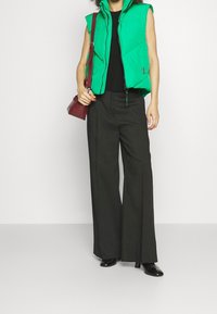 Groen gewatteerd mouwloos vest met rits aan de voorkant, gecombineerd met zwarte, hooggetailleerde wijde broekspijpen en zwarte laarzen met hak. Draagt een kleine kastanjebruine tas.