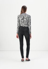 Vaqueros ajustados negros de cintura alta, combinados con una blusa blanca de manga larga que presenta un audaz diseño de estampado de cebra negro.