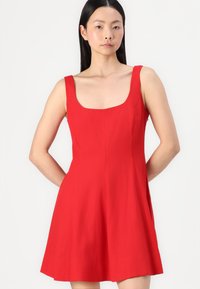 Robe sans manches rouge avec un décolleté carré, corsage ajusté et jupe évasée, fabriquée en tissu léger, présentant des lignes épurées et sans motifs visibles.