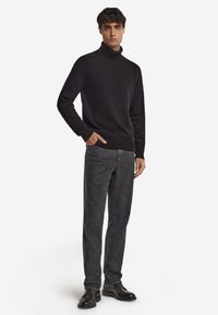 Czarny sweter z golfem z miękkiej tkaniny, z prążkowanymi mankietami i dołem, zestawiony z ciemnoszarymi, teksturowanymi spodniami oraz czarnymi butami.