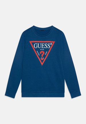 Niebieska koszulka z długim rękawem i okrągłym dekoltem, z czerwonym trójkątem z napisem "GUESS U.S.A." oraz logo znaku zapytania w kolorach białym i czerwonym na piersi.