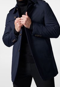 Manteau bleu marine au design structuré, comprenant un col, des boutons décoratifs et une fermeture simple boutonnage, fabriqué dans un tissu lisse.