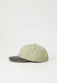 Green fabric cap with a gray-brimmed peak. Features six ventilation eyelets and stitched detailing. Side tag accents overall design.