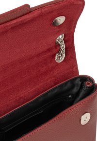 Portafoglio rosso in pelle con un esterno texturizzato, interno in suede a contrasto, chiusura a pressione in argento e tasca con zip. Presenta un accento a catena.