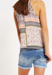 Top sin mangas multicolor con diseño floral y estampado, con cuello halter y corte holgado. Combinado con pantalones cortos de mezclilla.