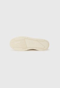Suela de zapatilla color crema con una superficie texturizada, que presenta surcos estampados y un logotipo de marca prominente grabado.