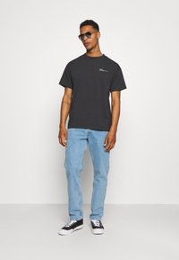 Camiseta de algodón negra con mangas cortas, que presenta un logo blanco minimalista; combinada con unos jeans de mezclilla azul claro y zapatillas negras.