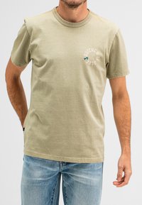 Olijfgroene katoenen T-shirt met korte mouwen, voorzien van een rond logo-ontwerp in blauw en beige op de linkerborst. Klassieke ronde halsstijl.