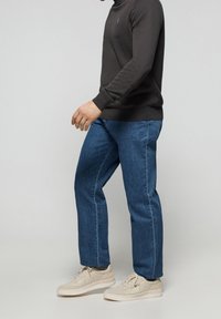 Ciemnoszara bluza, niebieskie jeansy o prostych nogawkach oraz beżowe trampki. Bluza ma prążkowany dekolt i mankiety. Jeansy mają klasyczną fakturę denimu.