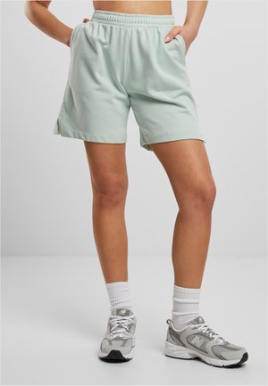 Person wearing light green elastic waist shorts and white New Balance sneakers with white crew socks against a plain background.