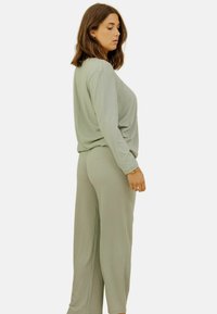 Ensemble loungewear côtes vert clair comprenant un haut à coupe décontractée et un pantalon fuselé, mettant en avant une texture de tissu douce et des lignes subtiles.