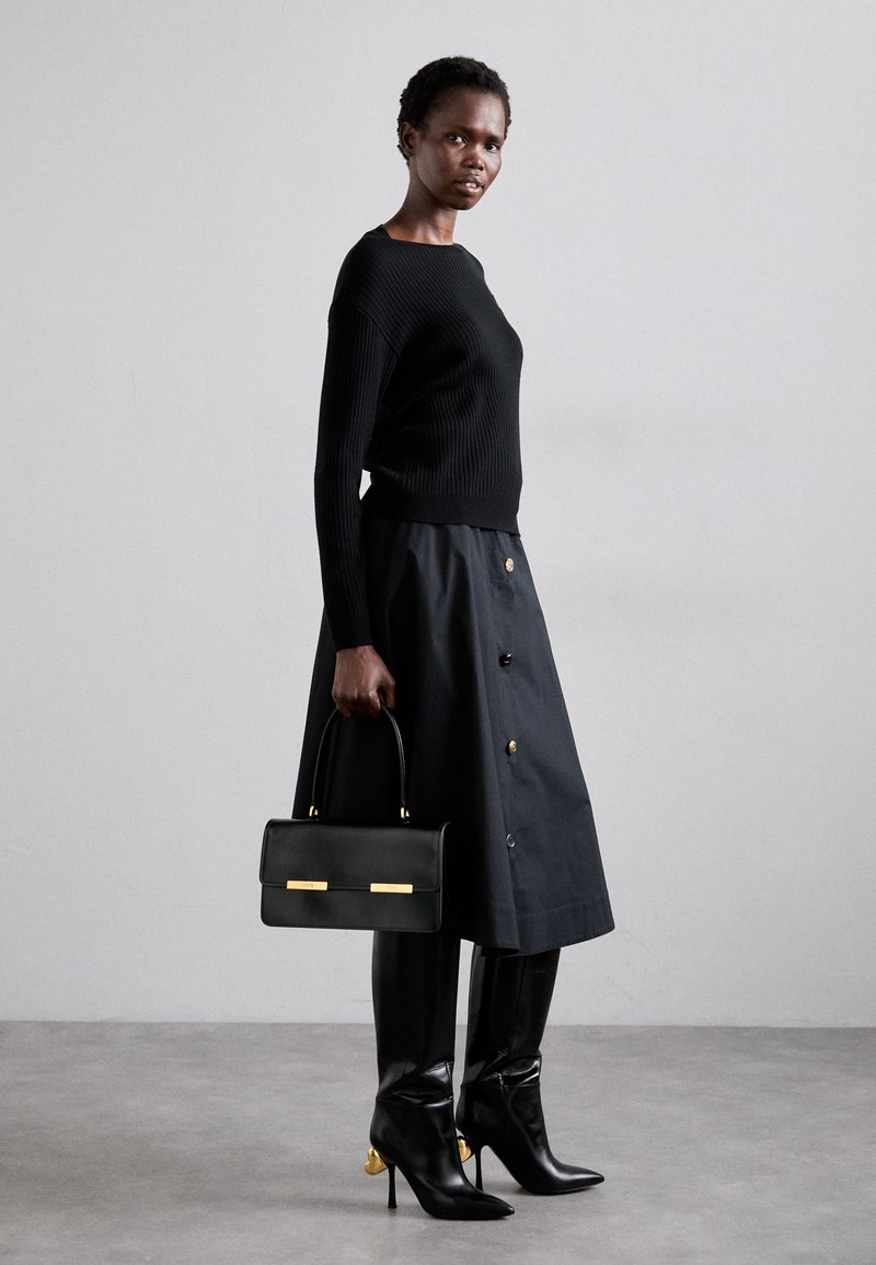 Maglione nero a coste, gonna nera fino al ginocchio con dettagli di bottoni, abbinata a stivali neri con tacco a spillo e dettagli in oro, portando una borsa nera.