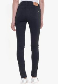 Jeans skinny negros con cintura alta, con una etiqueta de cuero en la parte posterior, dos bolsillos traseros y una textura de denim suave.