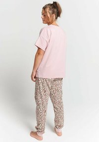 Pink cotton t-shirt with short sleeves paired with beige joggers featuring a pink and brown leopard print pattern. Relaxed fit, elastic cuffs.
