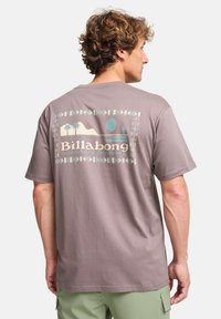 Grijze katoenen t-shirt met een grafische afdruk van palmbomen, bergen en een cirkel. Korte mouwen, losse pasvorm en ronde hals.