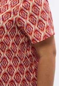 Κοντομάνικη μπλούζα με υφή υφάσματος και γεωμετρικό μοτίβο σε κόκκινο, πορτοκαλί και λεβαντίν σε κρεμ φόντο.