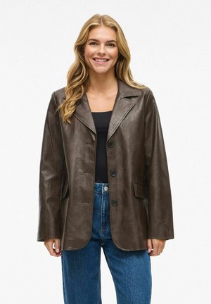 Blazer en cuir marron avec col à revers, deux poches avant et fermeture à bouton, associé à un jean bleu taille haute. Texture lisse.
