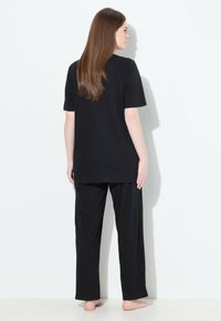 Conjunto de loungewear negro que incluye una camiseta de corte holgado con mangas cortas y pantalones largos de corte recto. Textura de tela suave y lisa.