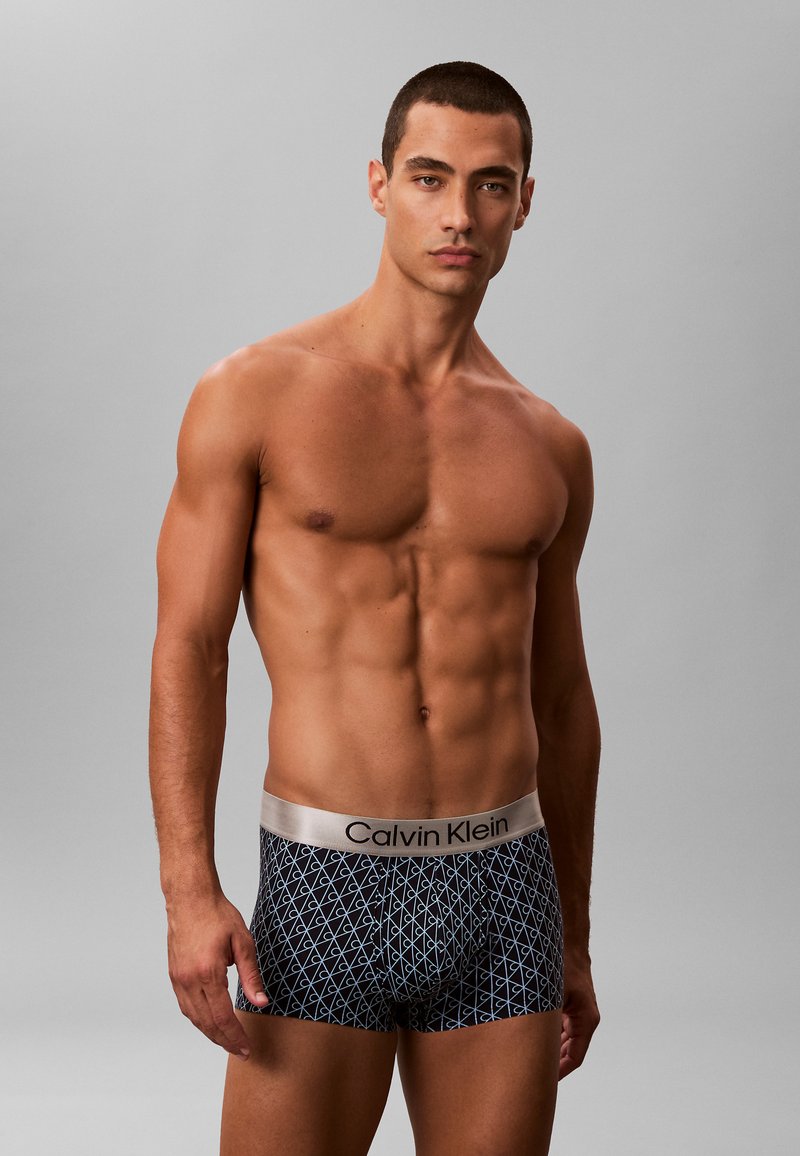 Boxers para hombre de Calvin Klein en negro con un patrón geométrico azul, con una cinturilla plateada con logo, fabricados en una suave mezcla de algodón.