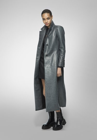 Long gray leather coat with a single-breasted design, notched collar, and front pockets. Worn over a black dress and paired with chunky black boots.