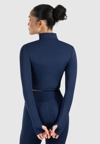 Marineblauwe lange mouwen cropped top van rekbaar materiaal, met een hoge kraag en duimgaten, gecombineerd met bijpassende strakke leggings.