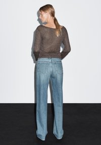 Hnědý pletený svetr se širokým výstřihem v kombinaci se světle modrými džíny s vysokým pasem, volným střihem, pěti kapsami a olemovanými okraji.