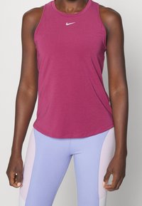 Fioletowy top na ramiączkach z okrągłym dekoltem i bez rękawów. Na piersi małe białe logo Nike. Gładki materiał o luźnym kroju.