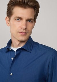 Camisa azul de botones hecha de un tejido ligero, con un cuello clásico y una textura sutil. Exhibida sobre un fondo neutro.