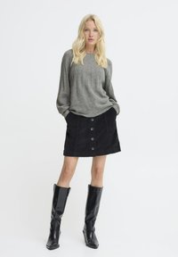 Maglione grigio a coste, gonna in velluto a coste nera con chiusura frontale a bottoni e stivali neri al ginocchio. Stile semplice e strutturato.