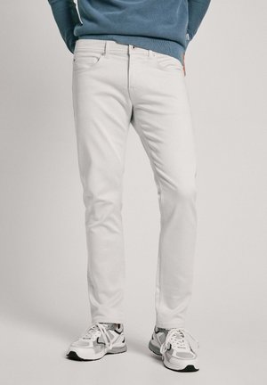 Weiße Jeans mit schlanker Passform, Fünf-Taschen-Design, gestickten Details, kombiniert mit grauen und weißen sportlichen Sneakern.
