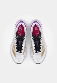 Scarpe da corsa bianche con strisce dorate, lacci neri e una soletta viola e rosa con il testo "ADIZERO". Design in rete leggero.
